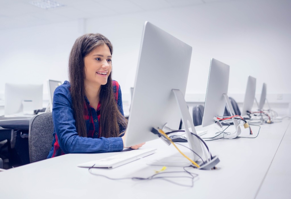 Student smiling while working at a computer in a modern classroom lab.