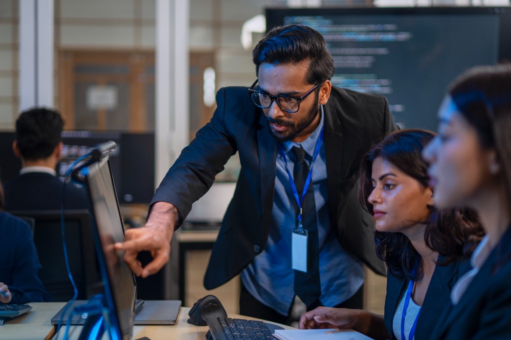 IT professionals collaborating at a workstation, reviewing code on a monitor in a modern office.